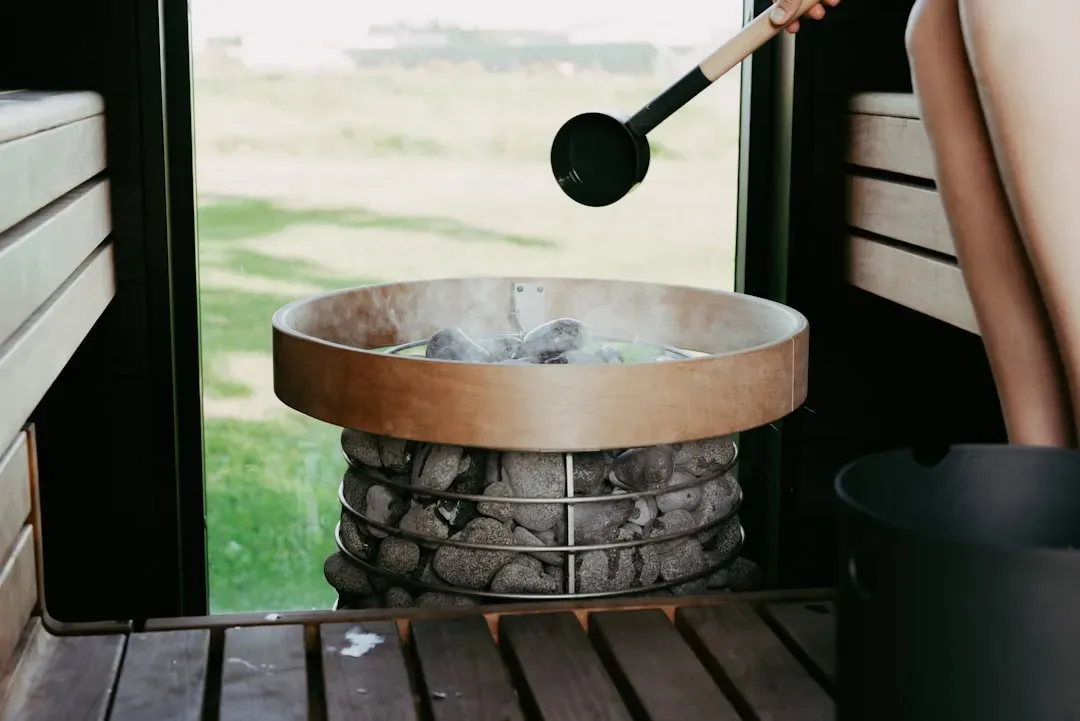 Hot sauna stones with water droplets creating steam in dramatic warm lighting, illustrating heat therapy benefits