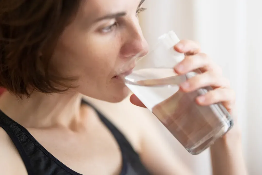 Person hydrating with water bottle before sauna session, demonstrating proper pre-sauna preparation for maximizing sauna bene