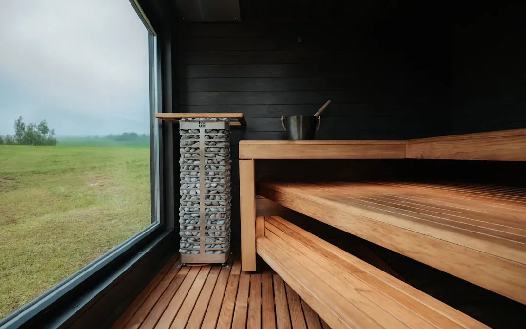 Person relaxing in sauna with yoga mat and meditation cushion nearby, surrounded by plants and natural light for holistic str