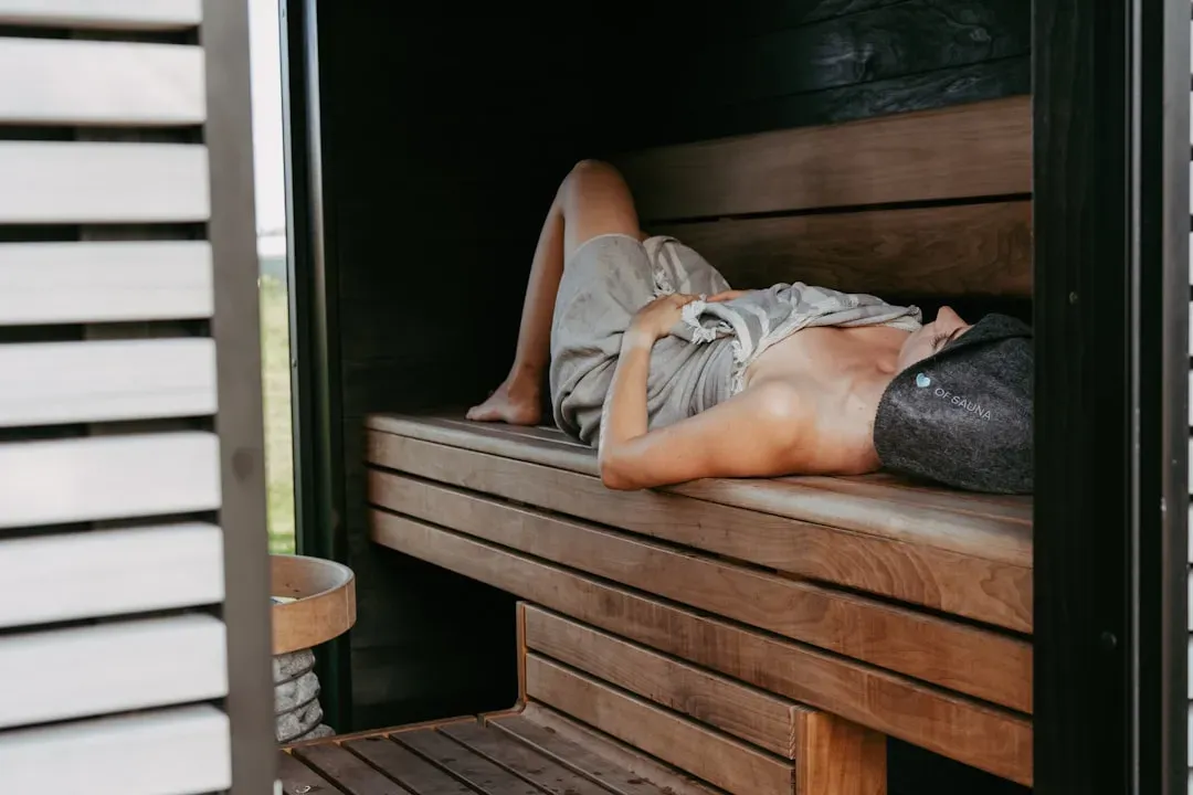 Beginner demonstrating proper sauna posture and positioning on wooden bench for safe, effective sauna use
