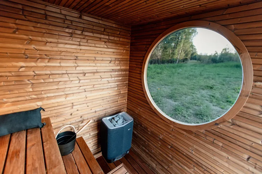 Person relaxing in modern infrared sauna cabin with glowing heating elements and dark wood paneling, demonstrating dry sauna 