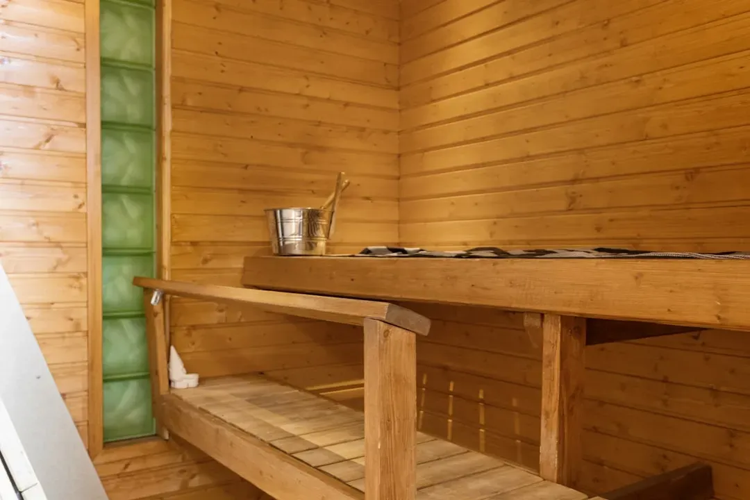 Traditional Finnish sauna interior with wooden benches, glowing hot stones in wood stove, and steam rising in warm amber ligh