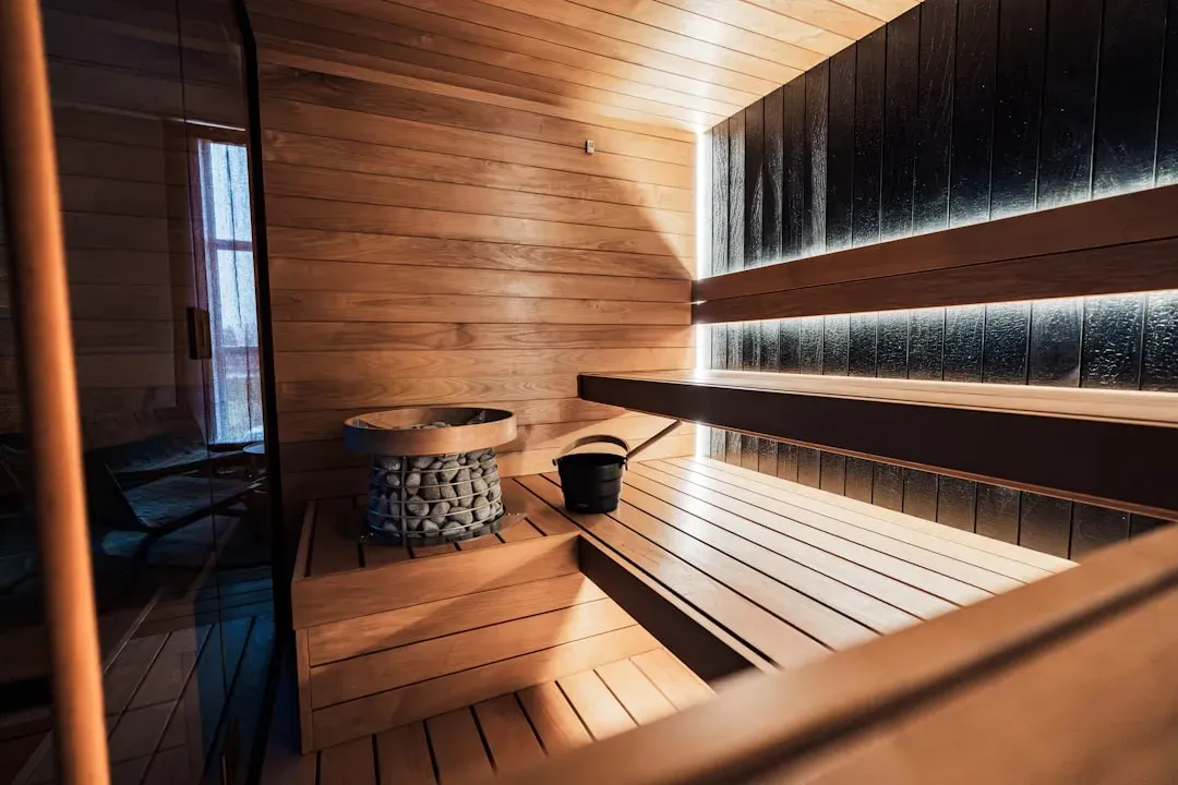 Modern Finnish home sauna interior with wooden benches, heated stones, and steam rising from the heater