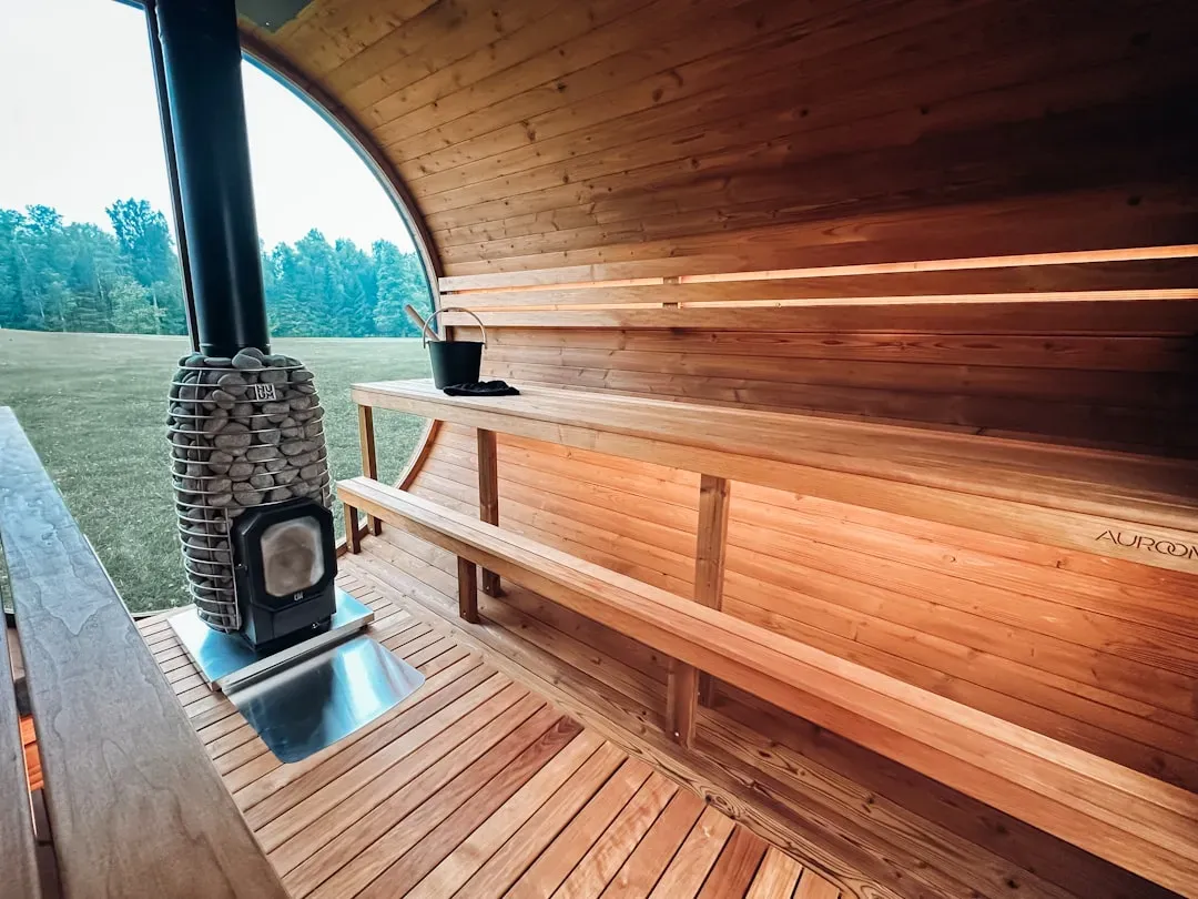 Traditional wooden sauna interior with cedar walls, bench seating, warm lighting, thermometer at 180°F, and steam for optimal