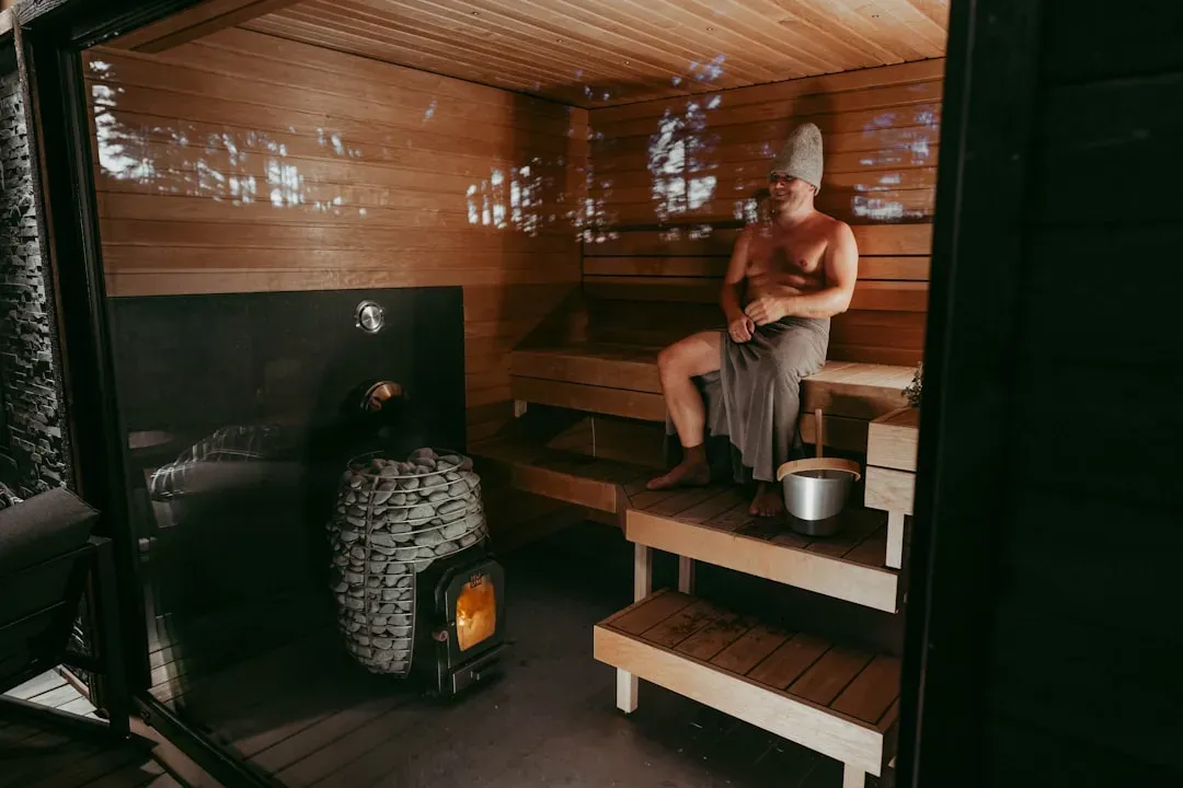 Mature man relaxing in wooden sauna with steam, experiencing sauna benefits for men including testosterone and heart health i