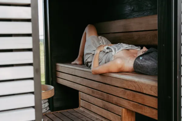 Person relaxing in traditional wooden sauna with steam rising, experiencing sauna benefits for hair and overall wellness in w