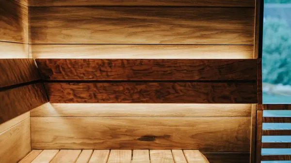 Finished home sauna interior with cedar wood paneling, tiered wooden benches, warm lighting, and traditional heater with rock